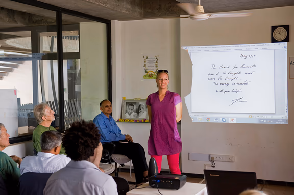 Inge van Alphen addressing the audience. The Mother's message says: The lands for Auroville are to be bought and can be bought. The money is needed