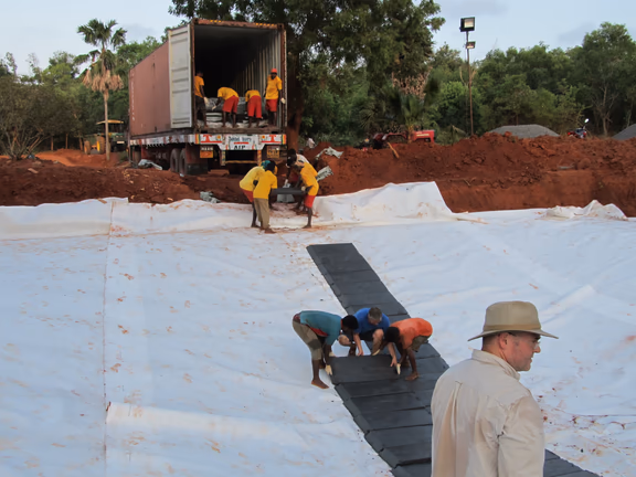 Laying compacted clay slabs on a geotextile under-layer in one of the six mini test ponds at Matrimandir